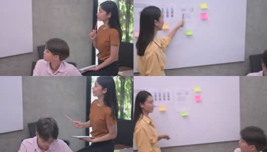 年轻的亚洲女性在白板上展示自己的想法，而她的合作团队在室内观看。商业女性一起头脑风暴高清在线视频素材下载