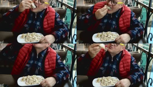 老人坐在餐厅或咖啡馆的桌边用手吃khinkali或土耳其馄饨。高清在线视频素材下载
