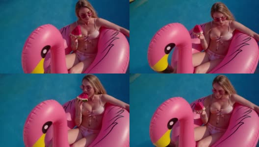 年轻女子吃着西瓜，漂浮在粉红色的火烈鸟充气上高清在线视频素材下载