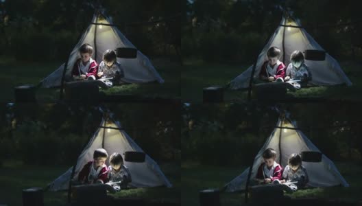可爱的小弟弟们，晚上在帐篷里玩平板电脑和电话高清在线视频素材下载