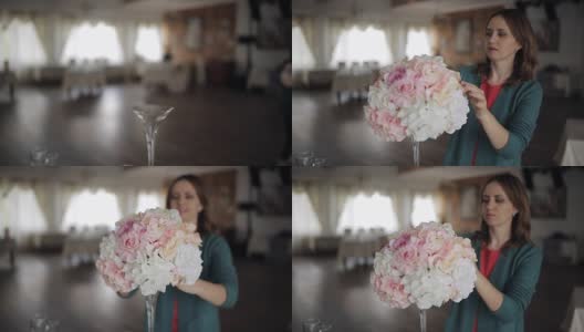年轻的女人纠正在桌子上的花的安排，花在高的玻璃花瓶，一个节日的桌子装饰，婚礼花束高清在线视频素材下载