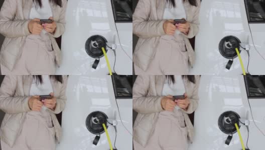 一名女子拿着智能手机在附近为电动车充电并检查电池状态。在户外公共充电站充电的车辆。汽车共享的概念高清在线视频素材下载