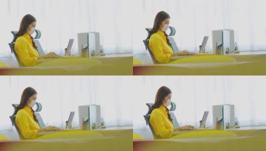 在现代办公室或联合办公空间创业的亚洲女性穿着黄色衬衫，戴着外科口罩，与电脑笔记本思考以获得想法和需求的新常态高清在线视频素材下载