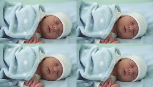 新生儿脸部肖像的特写，在白蓝色的背景上甜蜜地睡觉的早期日子。在帽子上的生命开始分钟的孩子。婴儿，分娩，出生的最初时刻，开始的概念高清在线视频素材下载
