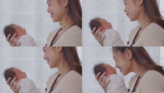 美丽迷人的亚洲妈妈抱着刚出生的宝宝，亲吻着宝宝的鼻子，甜美可爱。快乐的妈妈和宝宝一起看着宝宝，带着爱微笑。母亲，婴儿，新生儿概念。慢动作高清在线视频素材下载