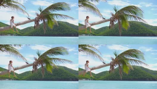 可爱的小女孩坐在棕榈树上在白色的海滩暑假高清在线视频素材下载