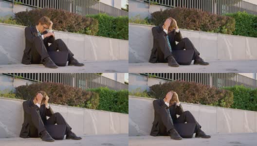 慢镜头:一个悲伤的男人坐在人行道上，双手抱头。高清在线视频素材下载