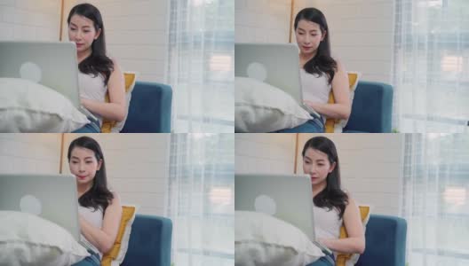 年轻的亚洲自由职业女性在家里的客厅休息时，用笔记本电脑查看社交媒体和喝咖啡。居家女性的生活方式概念。高清在线视频素材下载