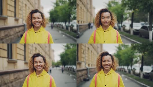快乐的非洲裔美国女孩微笑的慢动作肖像，看着镜头站在户外绿树和美丽的建筑为背景。高清在线视频素材下载