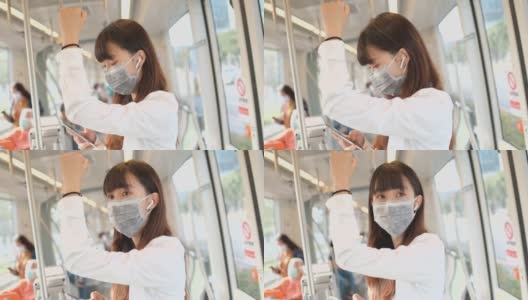 年轻的亚洲女性在捷运中使用智能手机，戴着保护面罩高清在线视频素材下载