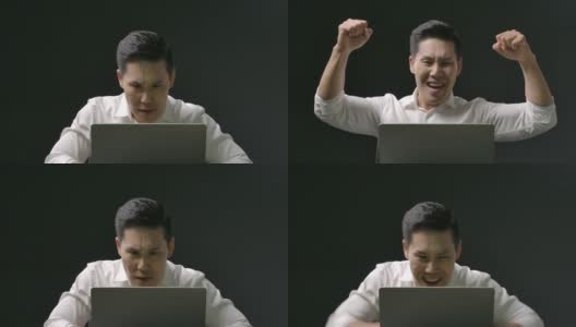 年轻的亚洲人看着笔记本电脑激动的情绪。一个帅哥在网上庆祝工作或学习的成功时刻。在隔离期间，穿着白衬衫的快乐男性在家。高清在线视频素材下载