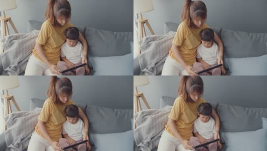 快乐快乐的亚洲家庭妈妈和可爱的孩子使用数字平板电脑兴趣卡通和看电影，在家里客厅的沙发上放松。高清在线视频素材下载