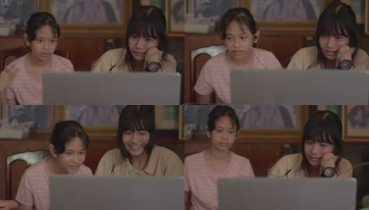 两个亚洲少女在家里用笔记本电脑从远程老师那里学习在线课程。泰国少女们坐在一起，戴着耳机在电脑屏幕上看电影。高清在线视频素材下载