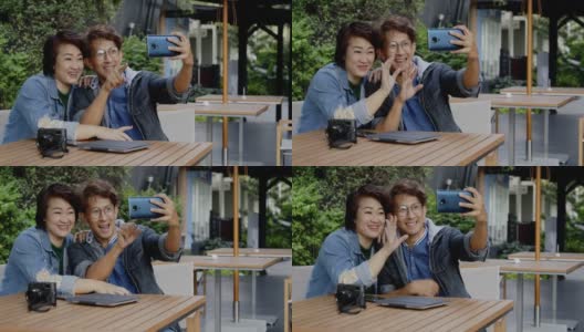 亚洲家庭情侣在夏日花园度假时用智能手机自拍。带着快乐的微笑坐在公园里视频聊天。休闲活动开放后的城市独立生活高清在线视频素材下载