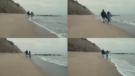在多云的日出中，一对快乐的情侣在狂野的海滩上奔跑高清在线视频素材下载