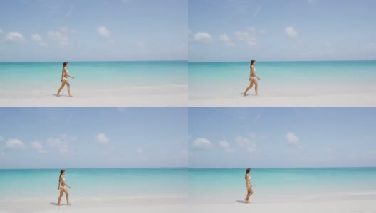 穿着白色比基尼的美女在海滩上散步。年轻的女性在暑假期间享受大自然。湛蓝天空下的海景。高清在线视频素材下载
