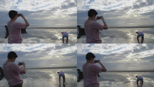 亚洲男孩在早上和家人在海滩上放松时用智能手机拍照，生活理念。高清在线视频素材下载