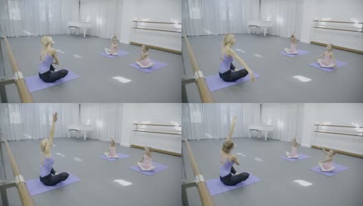 在芭蕾课上，教练和两个女孩坐在垫子上做芭蕾表演高清在线视频素材下载