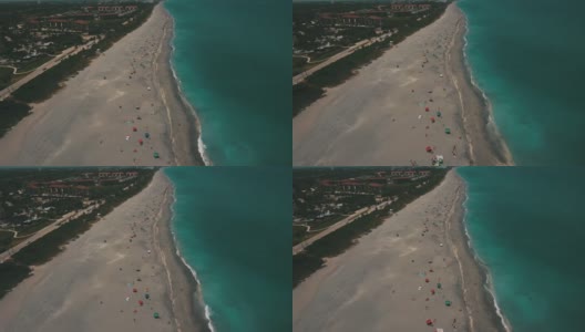 2021年3月春假和新冠肺炎期间，佛罗里达州朱诺海滩海滩海岸线上的彩色沙滩伞和人们的动态鸟瞰图高清在线视频素材下载