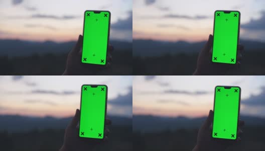 男人拿着智能手机的绿色屏幕与自然戏剧性的天空为背景，色度键高清在线视频素材下载