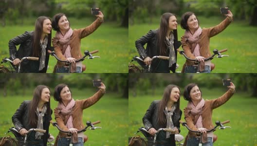 两名骑自行车的女性正在用智能手机拍照。年轻漂亮的黑发美女骑着自行车用手机给自己拍照高清在线视频素材下载