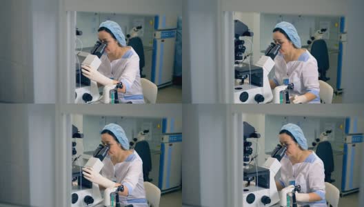 一个穿着手术服的女人正在使用实验室的显微镜。高清在线视频素材下载