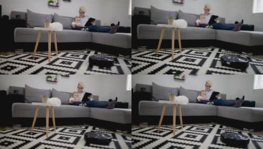 女人和男孩在用平板电脑，机器人在用吸尘器清扫家里的地板。现代生活方式的概念。高清在线视频素材下载
