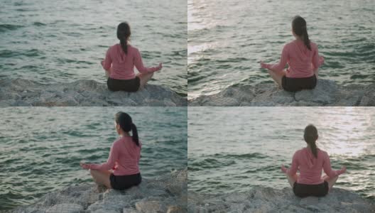 年轻美丽的运动女孩训练冥想坐在石头海边，而日落。高清在线视频素材下载