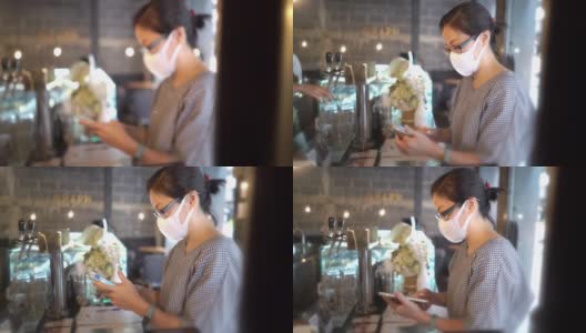 两名亚洲妇女戴着防护口罩在咖啡店用智能手机付款高清在线视频素材下载