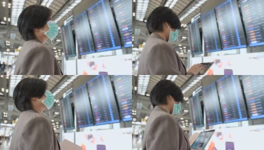 一名亚洲妇女戴着防毒面具看屏幕查看航班。高清在线视频素材下载