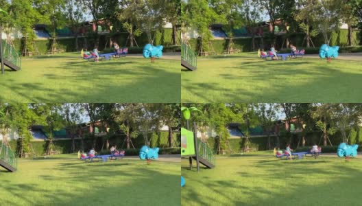 两个亚洲小女孩泰国兄弟姐妹一起在一个大的花园操场上玩跷跷板。孩子们在许多大树和绿草下进行户外运动。高清在线视频素材下载
