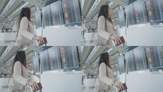一名亚洲女性旅客在机场，看着她旅行的航班带着行李，在屏幕上看到航班号就开始了新的旅行，旅行度假高清在线视频素材下载