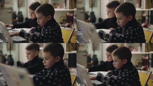 两个小男孩穿着温暖舒适的毛衣坐在编程课上的笔记本电脑前，试图学习如何使用这些小工具的慢镜头。高清在线视频素材下载