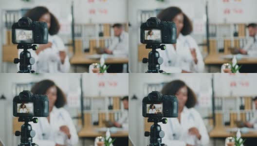 摄像机的观点漂亮自信经验丰富的30岁的黑皮肤女医生与在线观众谈论医学主题在现代诊所附近的胡子男同事高清在线视频素材下载