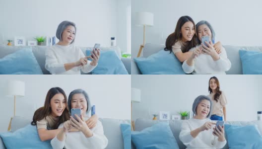 亚洲幸福家庭，年长的妈妈和女儿在家里用手机。漂亮迷人的女孩惊喜的坐在沙发上，年长的母亲和网上购物聊天在客厅的房子。高清在线视频素材下载