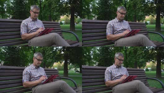 一名戴眼镜的男子在城市公园的平板电脑上浏览社交媒体高清在线视频素材下载