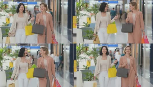 两个快乐的年轻女子走过购物中心，挎着购物袋的慢镜头高清在线视频素材下载