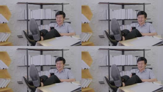 亚洲高级男子正坐在办公室里看着屏幕手机工作着，笑着开心的脸笑着开心的成功高清在线视频素材下载