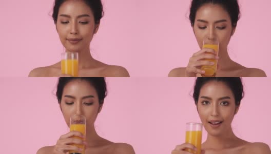 美丽的亚洲女孩喝橙汁。拿着玻璃杯的漂亮女孩，果汁和排毒饮料。饮料、保健、食品饮料的概念。高清在线视频素材下载