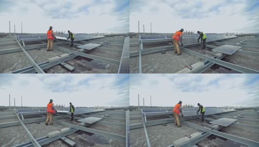 技术人员在金属底座上安装太阳能电池板。两名工人正在平屋顶上安装太阳能电池板。光伏板将太阳能转化为电能。高清在线视频素材下载