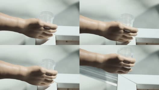 一个残疾人拿着一个塑料杯子喝水。一只义肢举起一杯水。独立完整的生活与假肢高清在线视频素材下载