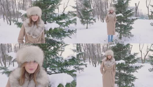 美丽的女人戴着皮帽看着相机在冬天的城市公园里白天在下雪的天气下飘落雪花，慢镜头高清在线视频素材下载
