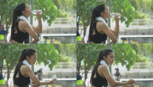 美丽的亚洲健身女人穿着运动服和毛巾在跑步后喝水休息。疲惫的女性在户外公园训练后休息高清在线视频素材下载