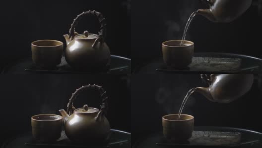 将热茶倒入玻璃茶壶和杯子中，木制背景上有蒸汽。健康热茶概念高清在线视频素材下载