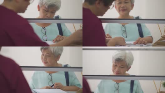亚洲华人老年妇女用信用卡支付医药费，女护士手持信用卡读卡器在诊所刷卡高清在线视频素材下载