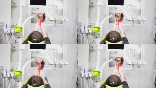 牙科椅上的年轻美女。手术后，她照照镜子。健康微笑的概念。高清在线视频素材下载