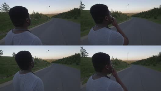 年轻的非洲裔美国人走在空旷的道路上，在日落时吸烟的背影高清在线视频素材下载