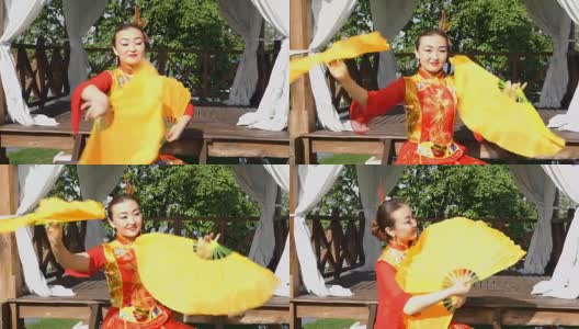 美丽的亚洲女人穿着红色的传统中国服装和两个大的黄色扇子跳舞。高清在线视频素材下载