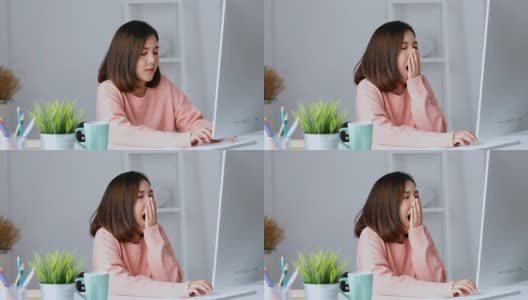 年轻的亚洲女人打哈欠，疲惫的工作与电脑在她的家庭办公室，在家里工作，人们在办公室的生活方式高清在线视频素材下载