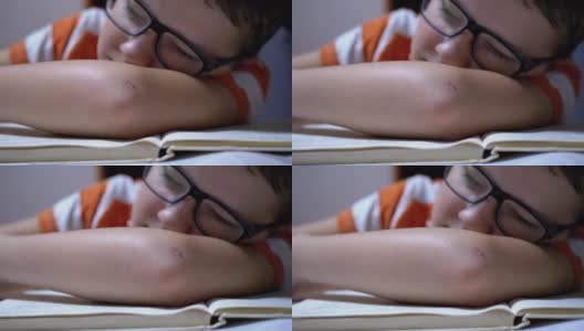 戴眼镜的好奇男孩在桌上看书时睡着了。疲劳、睡眠高清在线视频素材下载